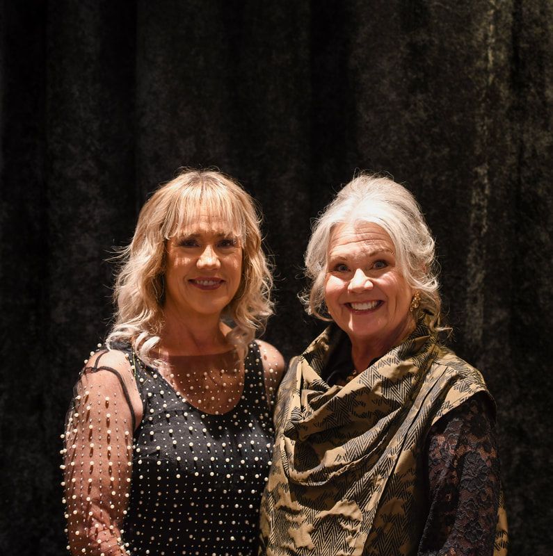 Two women posing for a picture in front of a black curtain