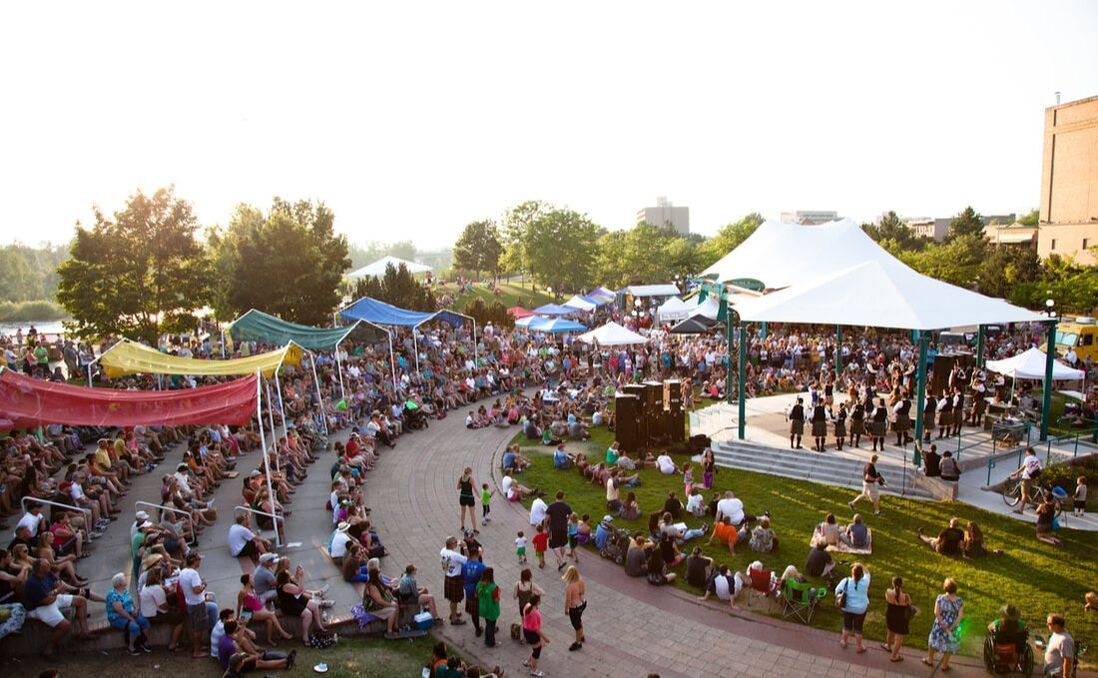 A large crowd of people are gathered in a park for a concert.