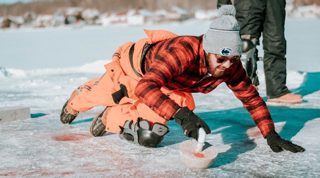 A man in a plaid shirt is kneeling on the ice.