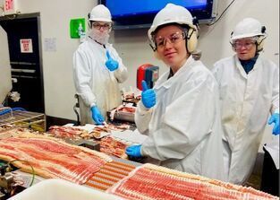 A woman in a lab coat is giving a thumbs up in a kitchen.