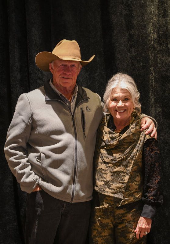 A man in a cowboy hat is standing next to a woman in a camouflage vest.