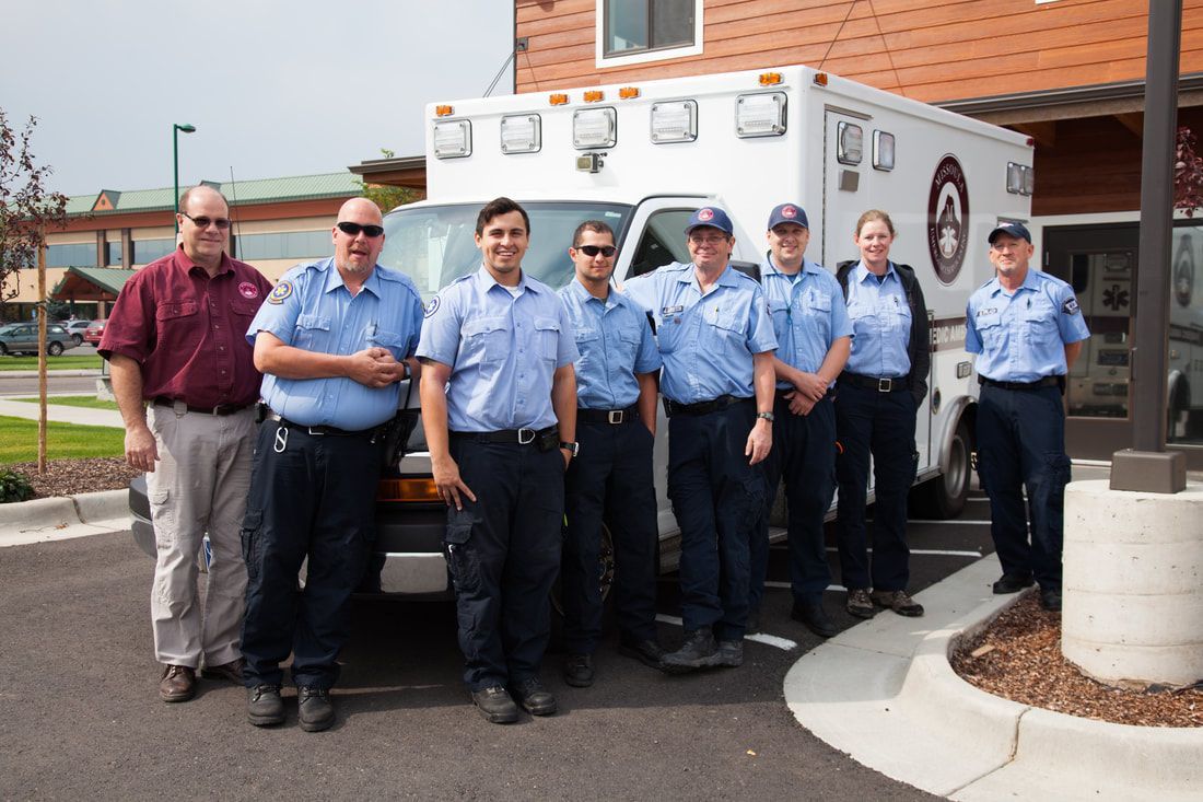 A group of paramedics are posing for a picture in front of an ambulance