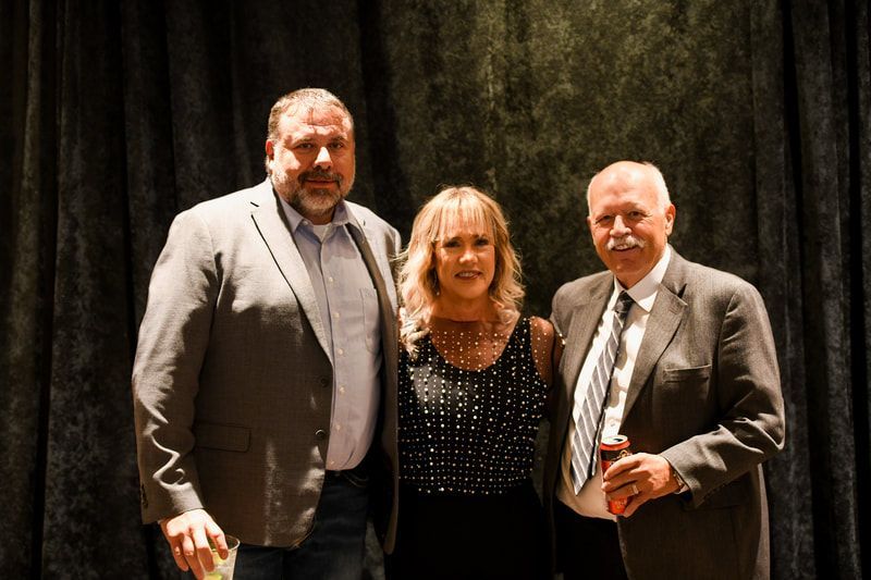 Three people are posing for a picture in front of a black curtain.