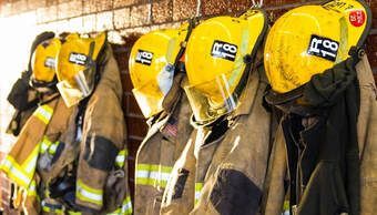 A row of firefighters ' uniforms and helmets hanging on a wall.