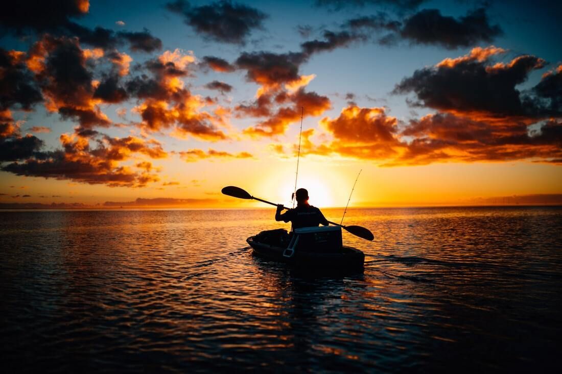 A man is rowing a kayak in the ocean at sunset.