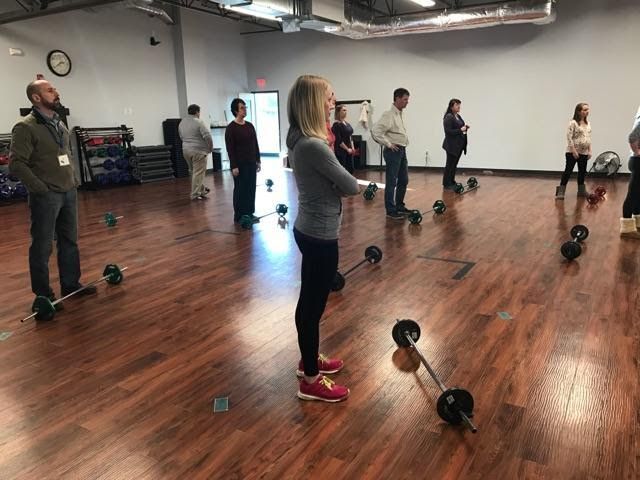 A group of people are standing in a gym with dumbbells.