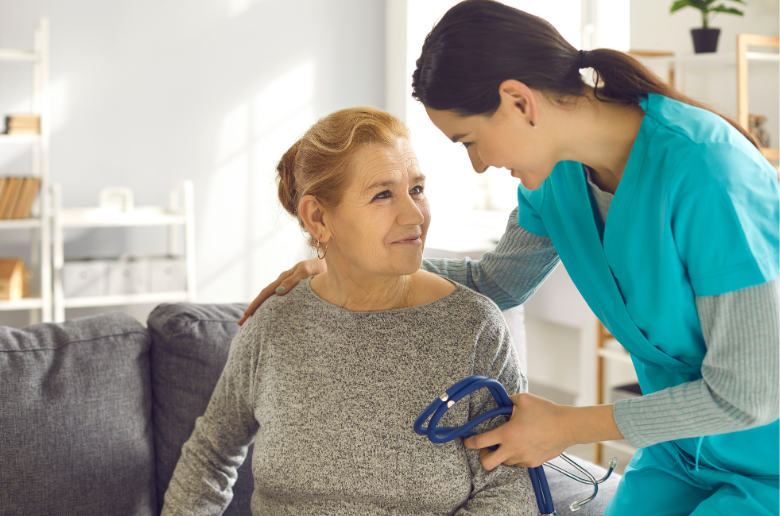 A nurse is talking to an elderly woman sitting on a couch.