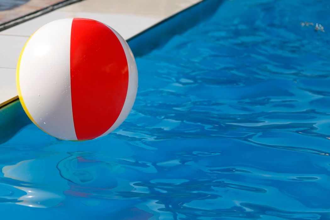 A red and white beach ball is floating in a swimming pool.