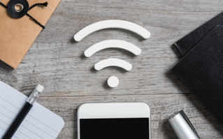 A cell phone is sitting on a wooden table with a wifi symbol above it.