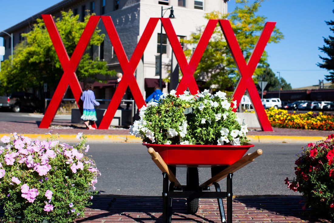 A red wheelbarrow filled with flowers sits in front of a red sign that says xxx