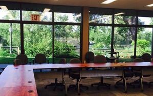 A conference room with a long table and chairs and an exit sign on the window.