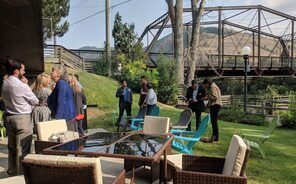 A group of people are standing around a table and chairs in a park.