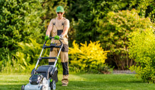 A man is using a lawn mower to cut the grass in a garden.