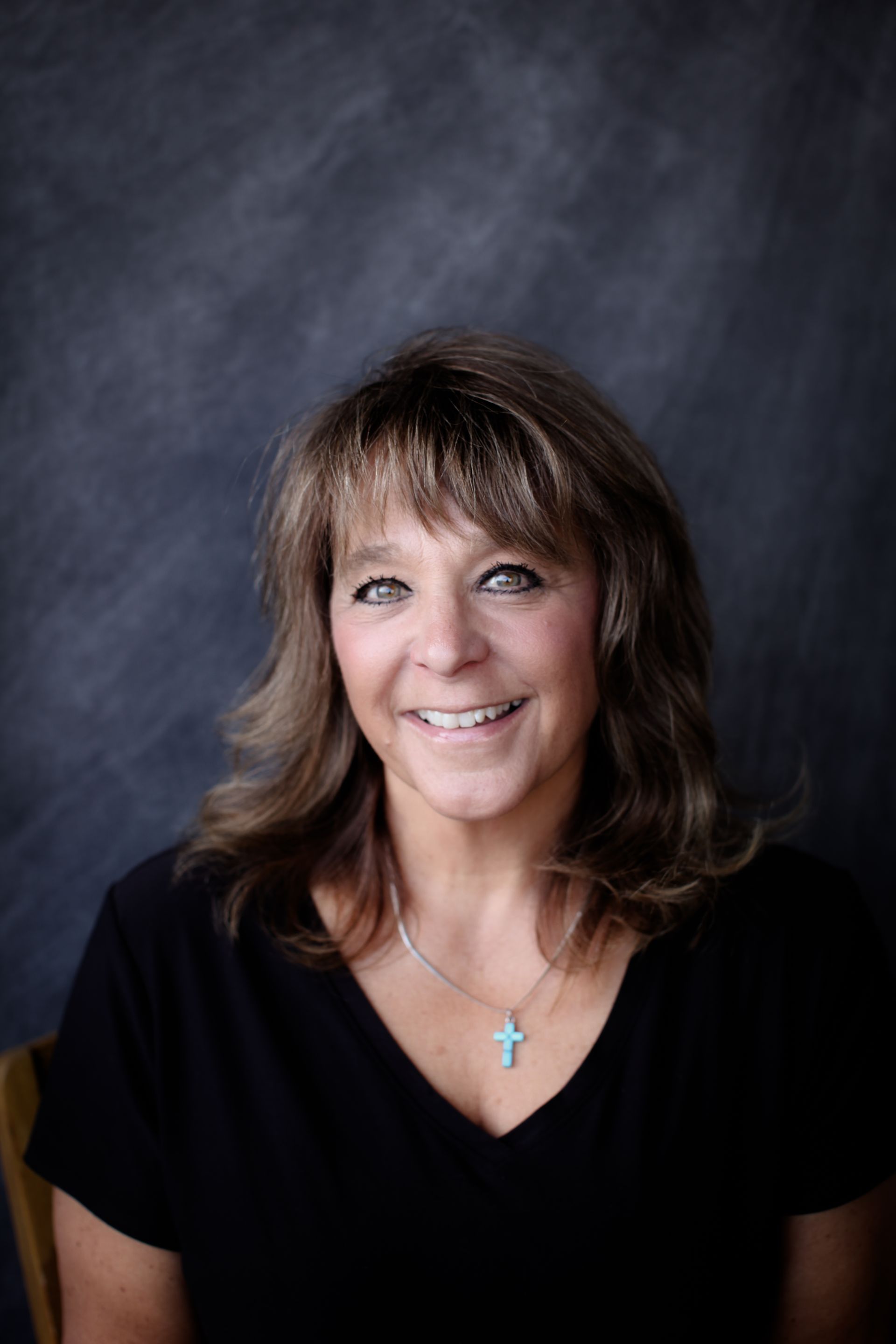 A woman wearing a black shirt and a cross necklace is smiling for the camera.