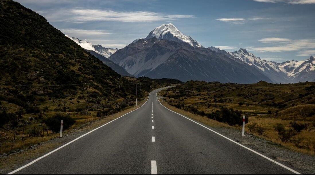 A road going through a mountainous area with a mountain in the background.
