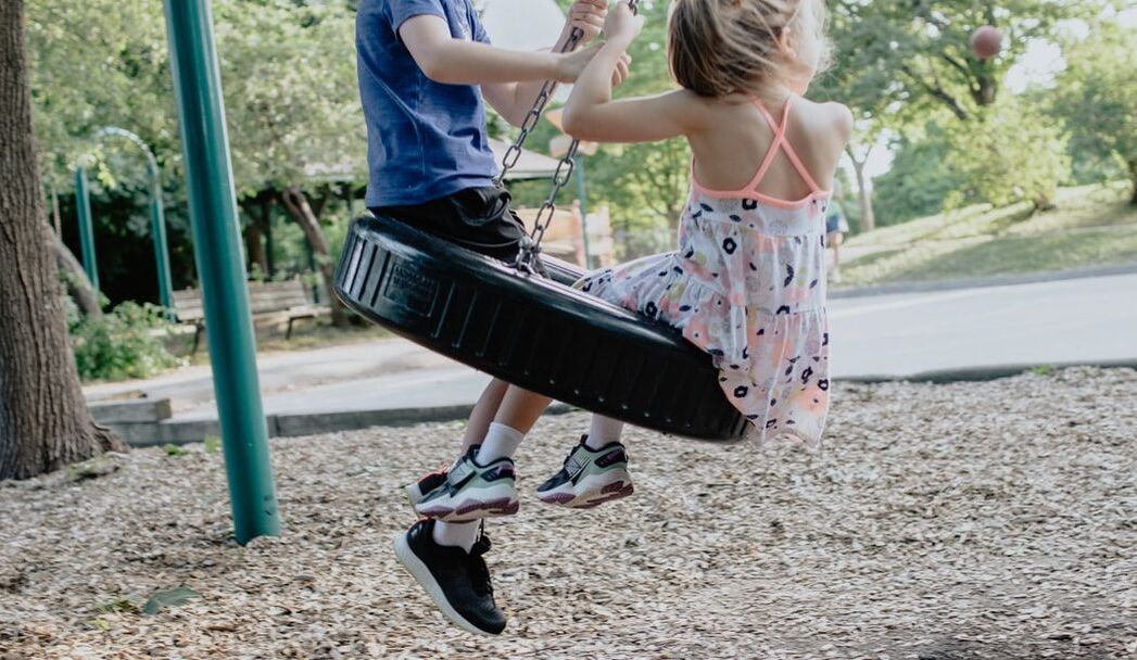 A boy and a girl are swinging on a tire swing in a park.