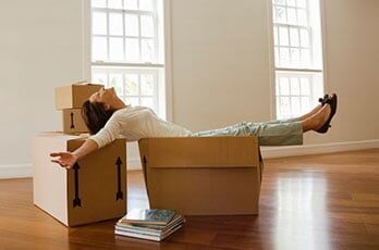 Mature woman sitting on boxes in empty room - packing supplies in CA