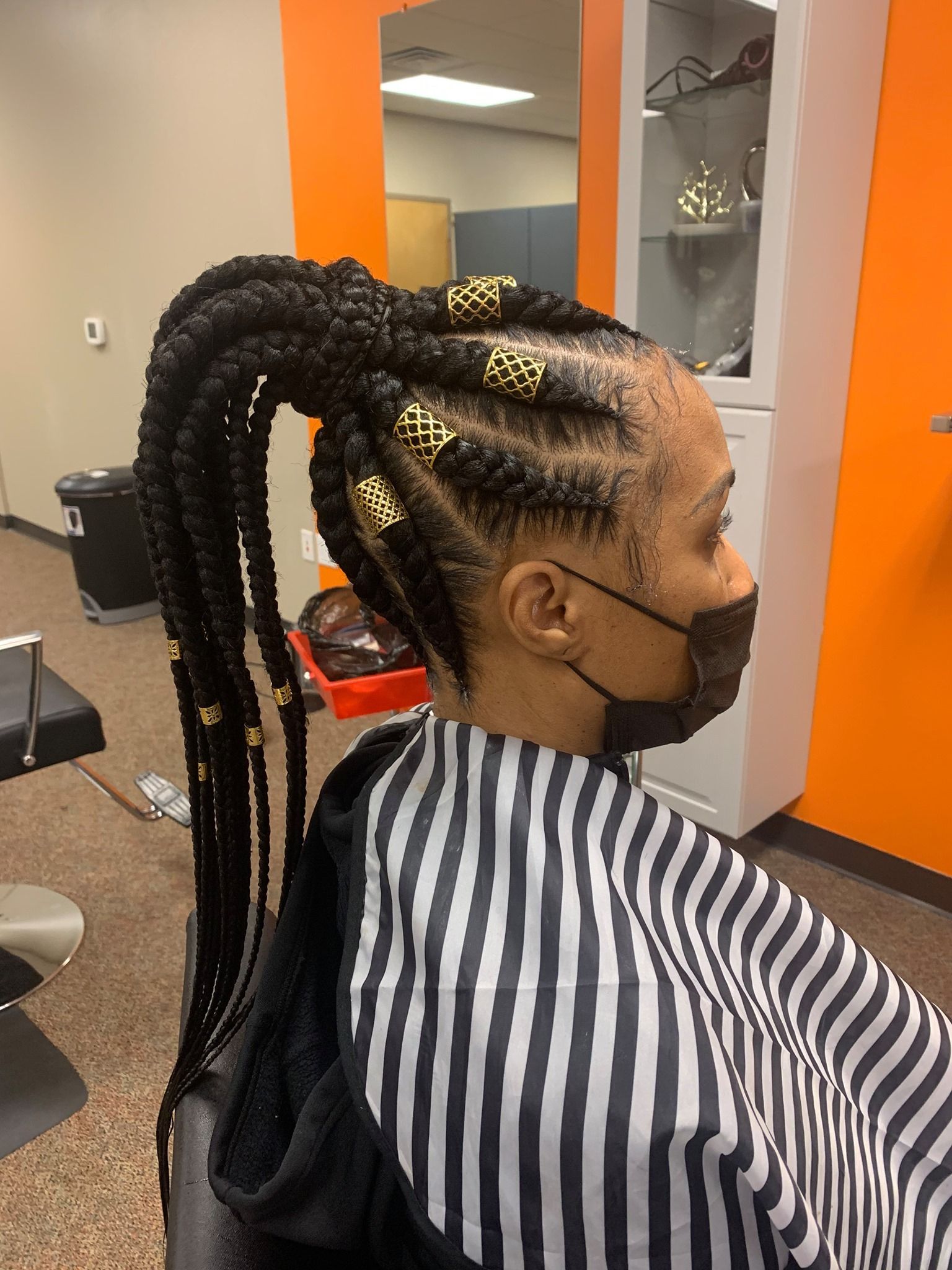 Woman with braided hairstyle, side profile, wearing a black face mask. Braids are adorned with gold beads.