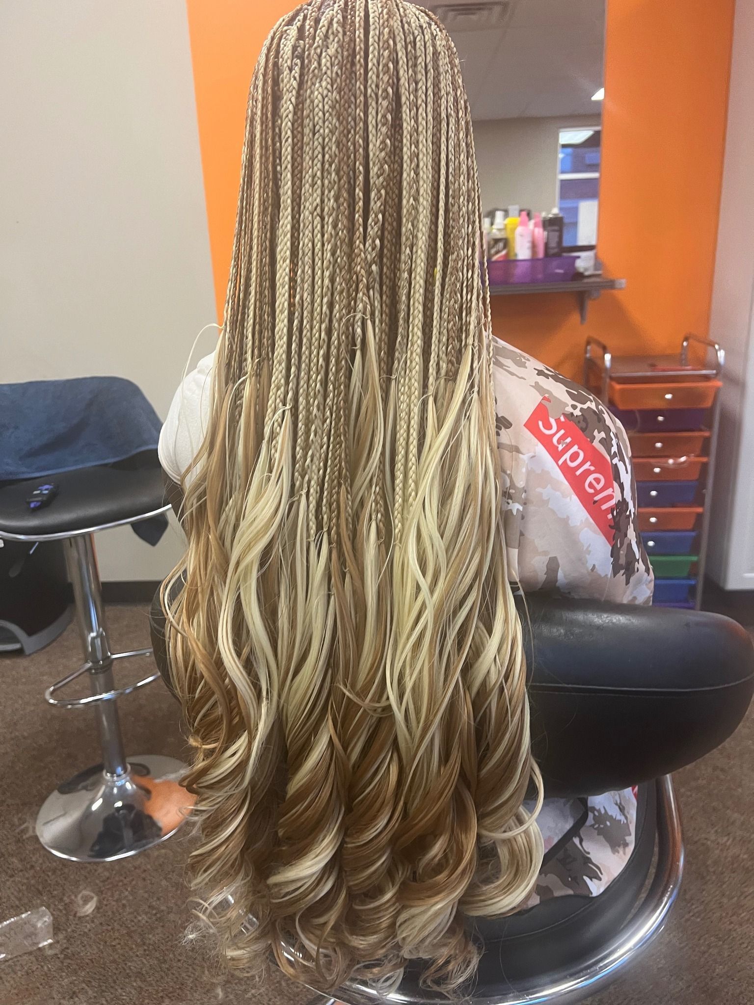 Woman with long blonde and brown box braids, sitting in a salon chair.