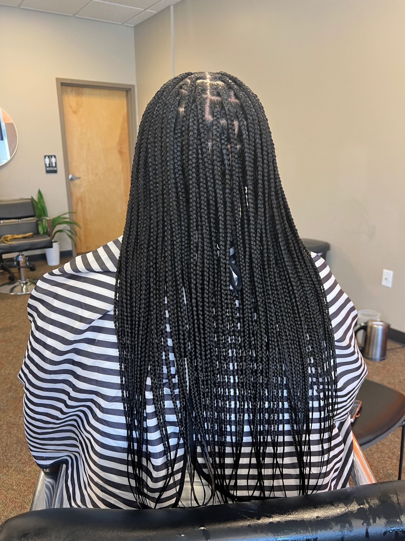 Person with long black box braids, wearing a black and white striped cape, in a salon.