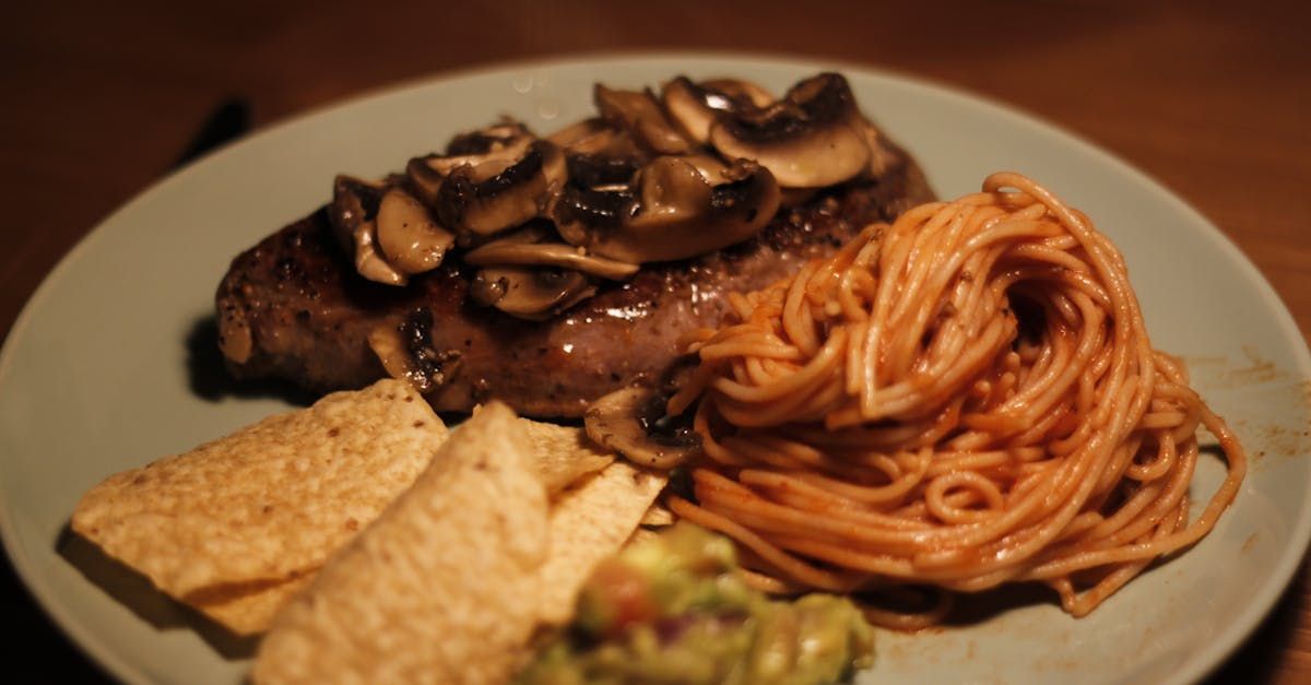 A plate of food with a steak , spaghetti , guacamole and tortilla chips.