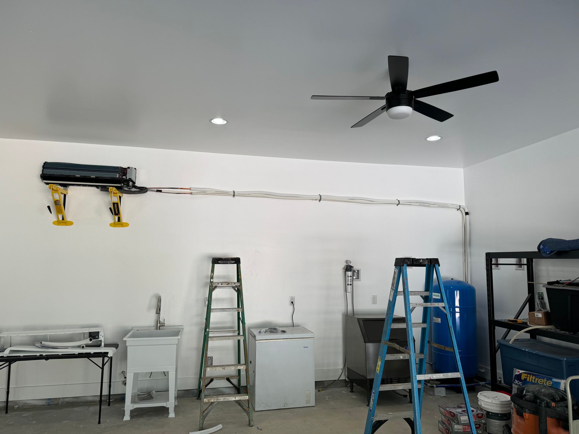 Garage interior with an AC unit mounted on the wall, a ceiling fan, and various appliances and tools.