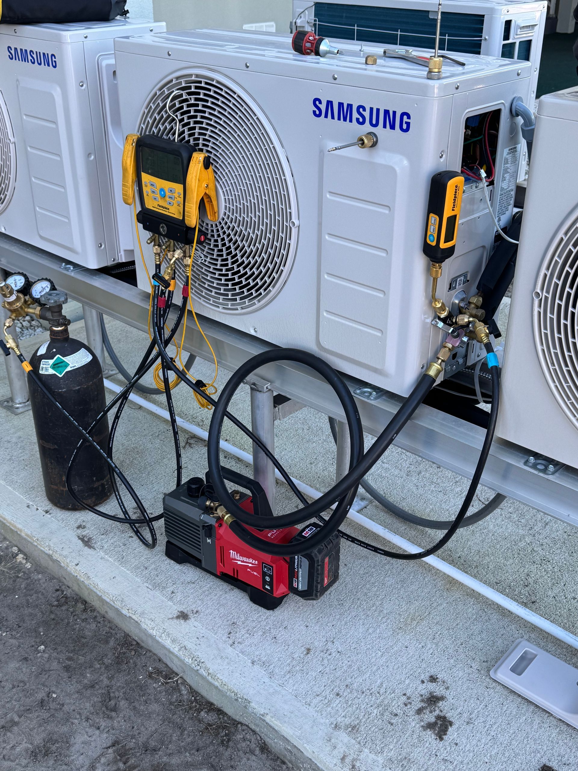 HVAC units with equipment: vacuum pump, gauges, and gas cylinder. Outdoor setting.