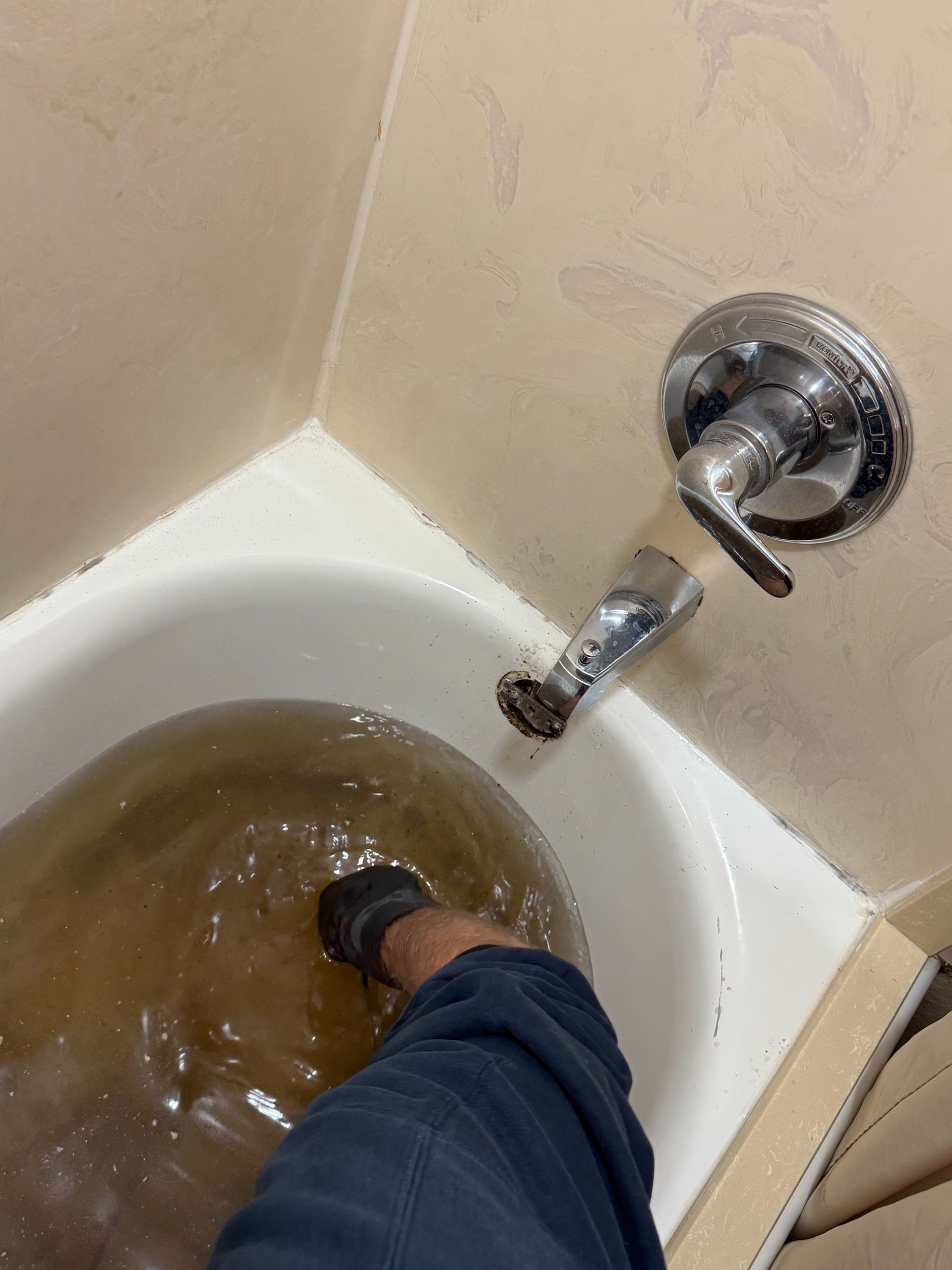 A foot in a bathtub filled with murky brown water near a faucet.