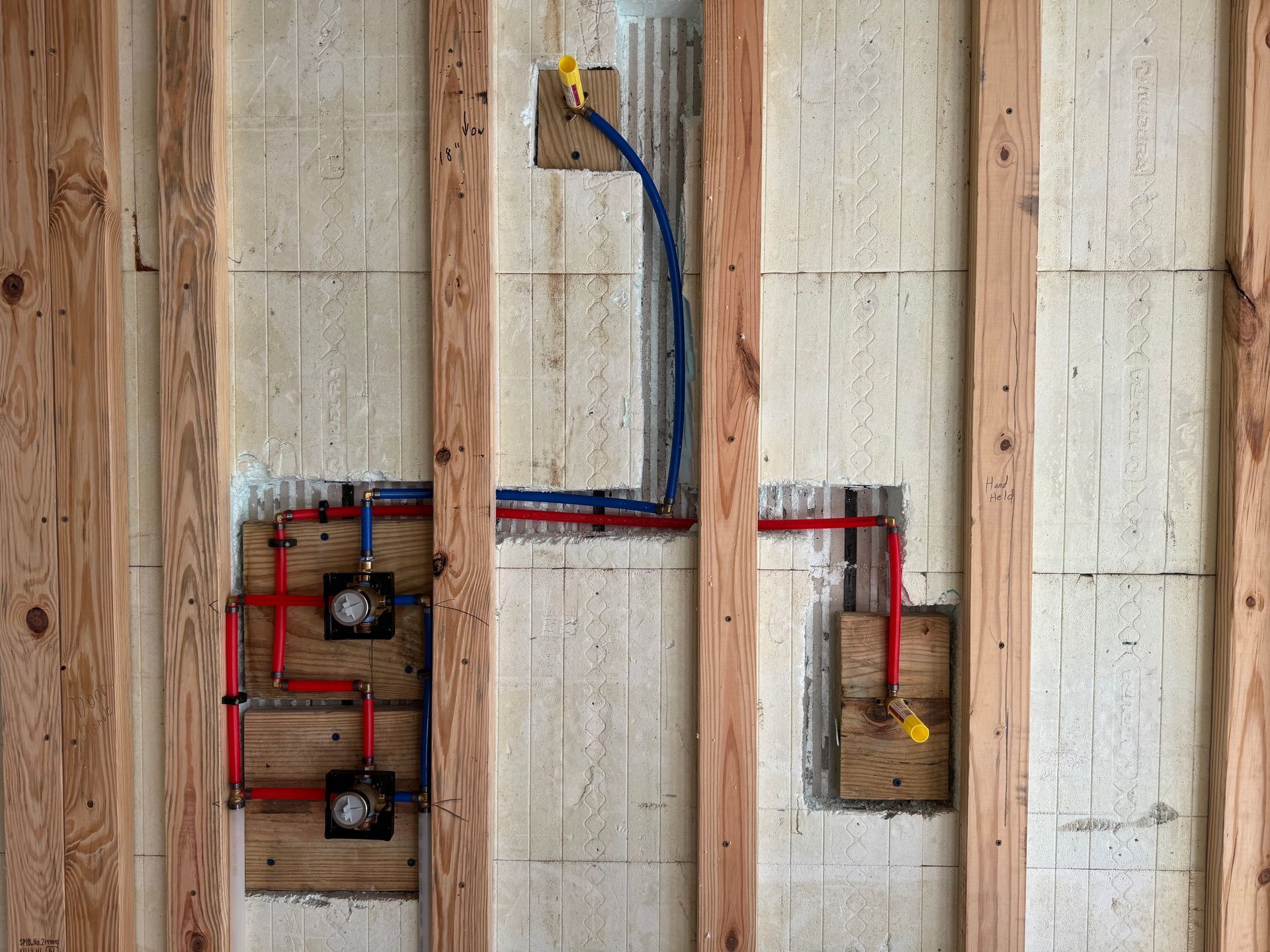 Framing with plumbing pipes: red and blue pipes connect to fixtures in a wall during construction.