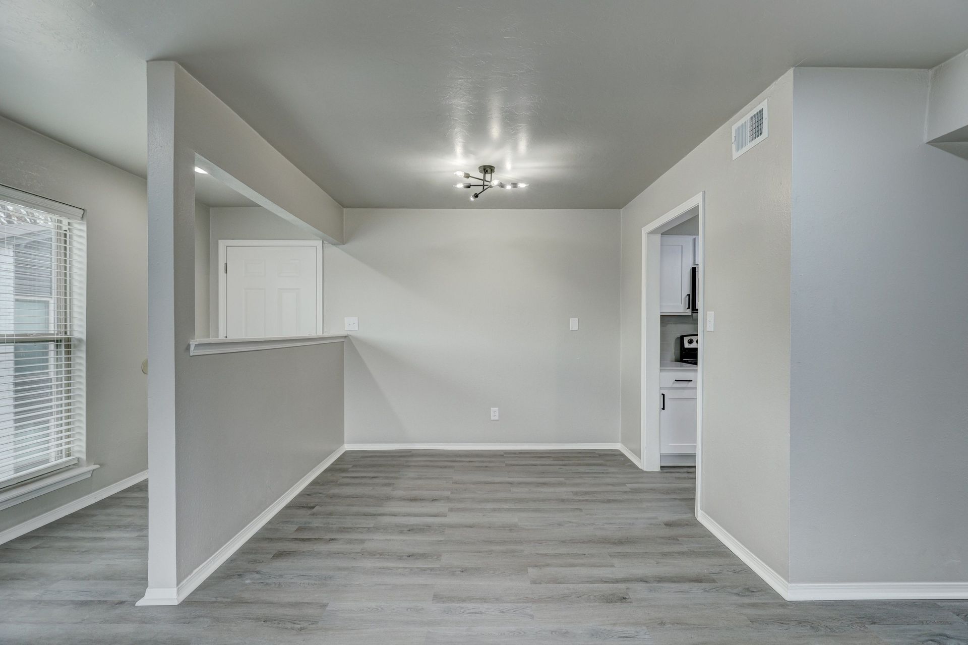 Empty dining area with gray walls, wood-look flooring, and a pass-through to a kitchen.