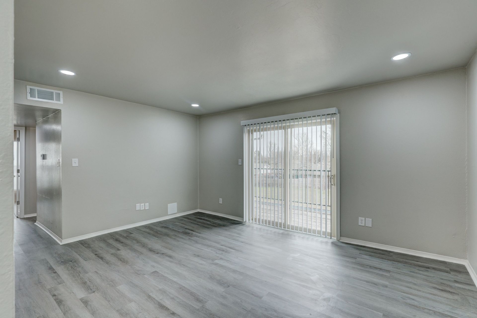 Empty living room with sliding glass doors and gray flooring.
