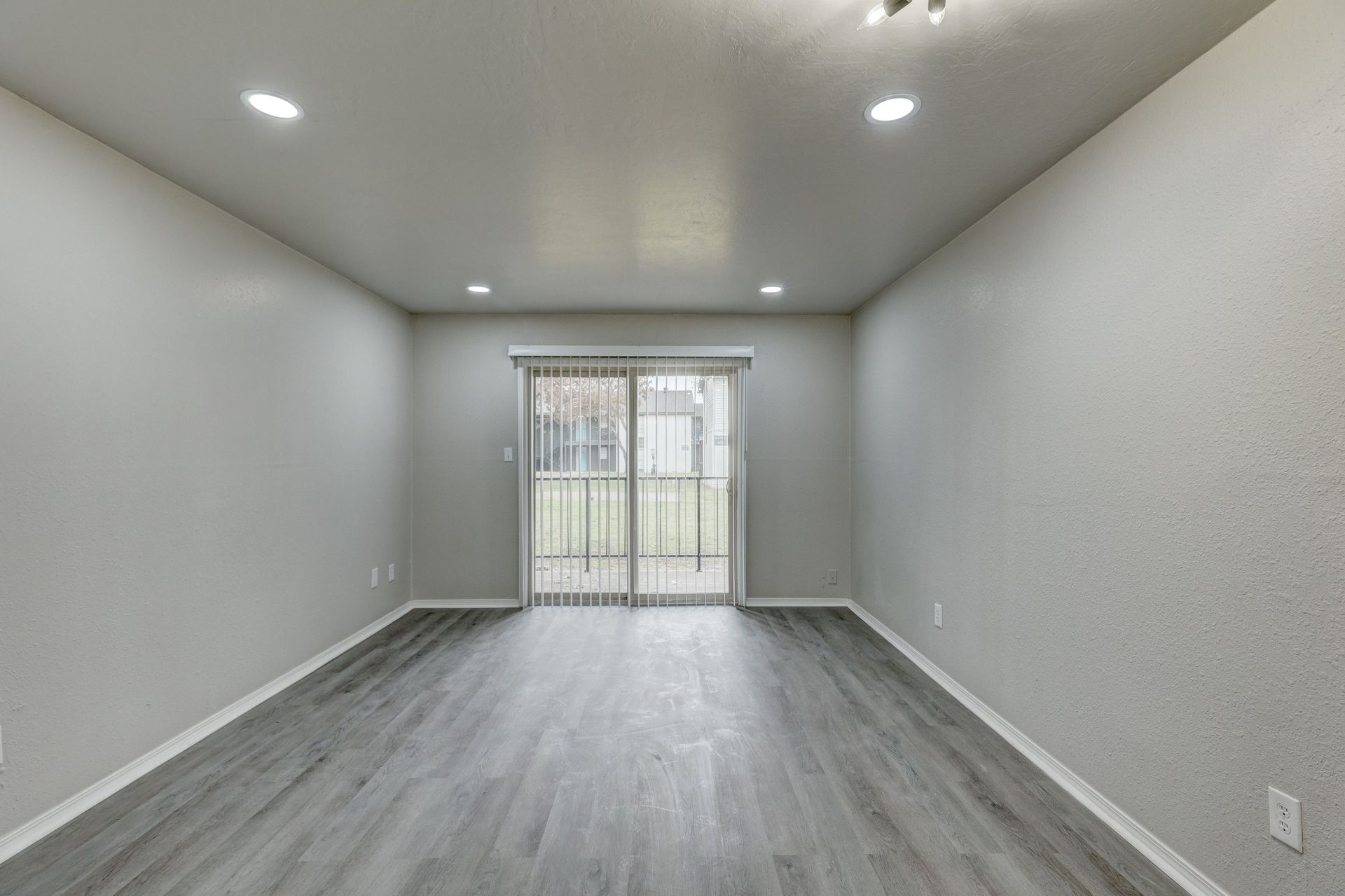 Empty room with gray walls and flooring, sliding glass doors to an outdoor patio.