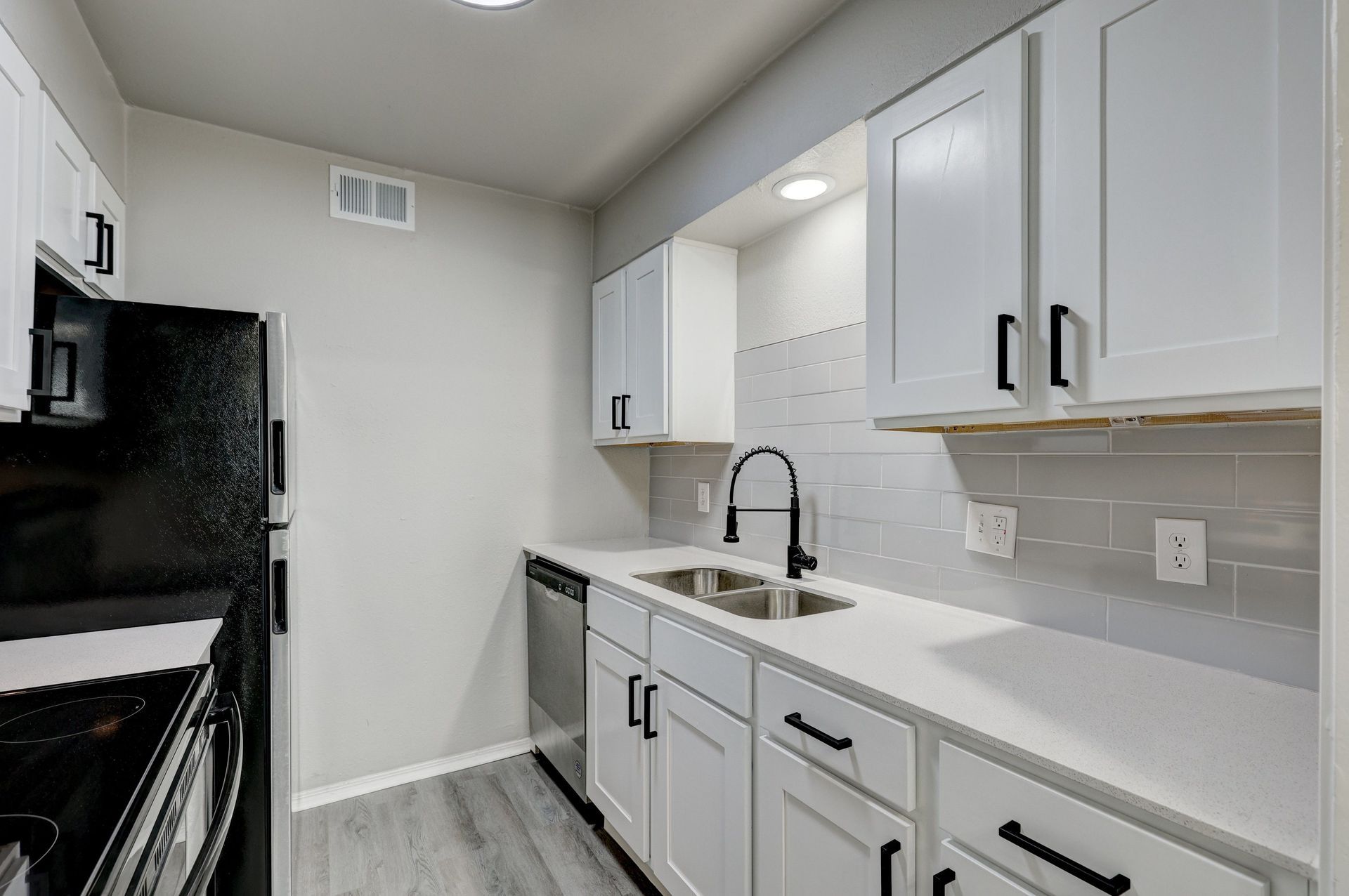 White kitchen with stainless steel appliances and gray backsplash.