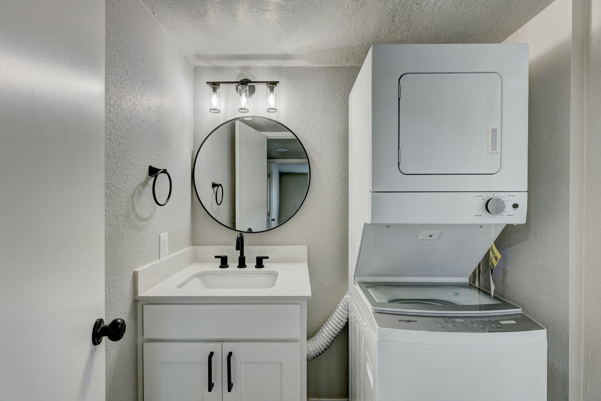 Small white bathroom with a stacked washer and dryer, sink, and mirror.