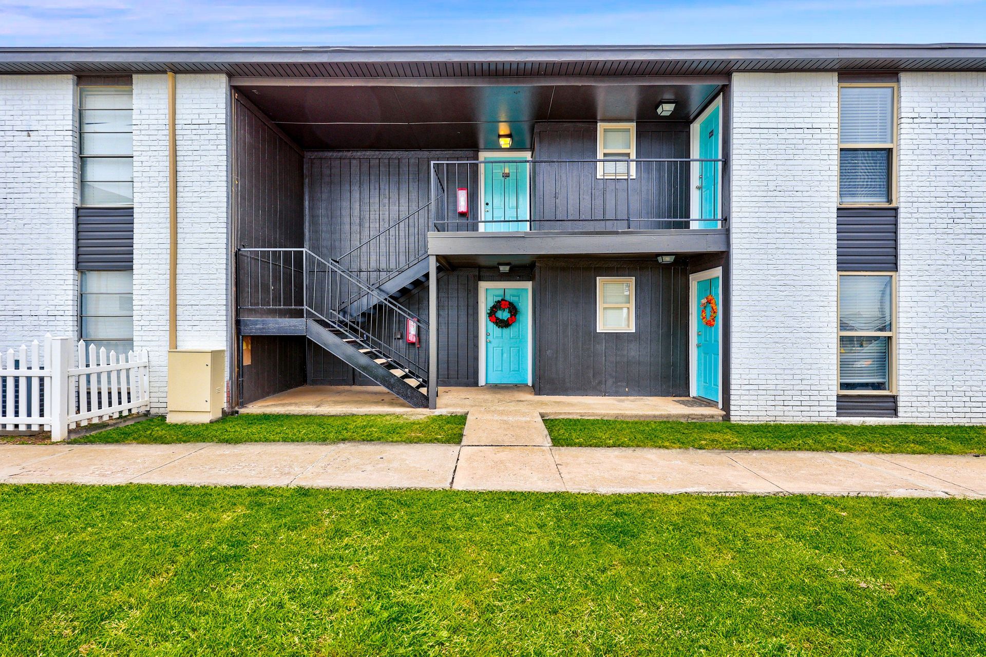 Two-story apartment building with turquoise doors, black stairwell, and green grass.