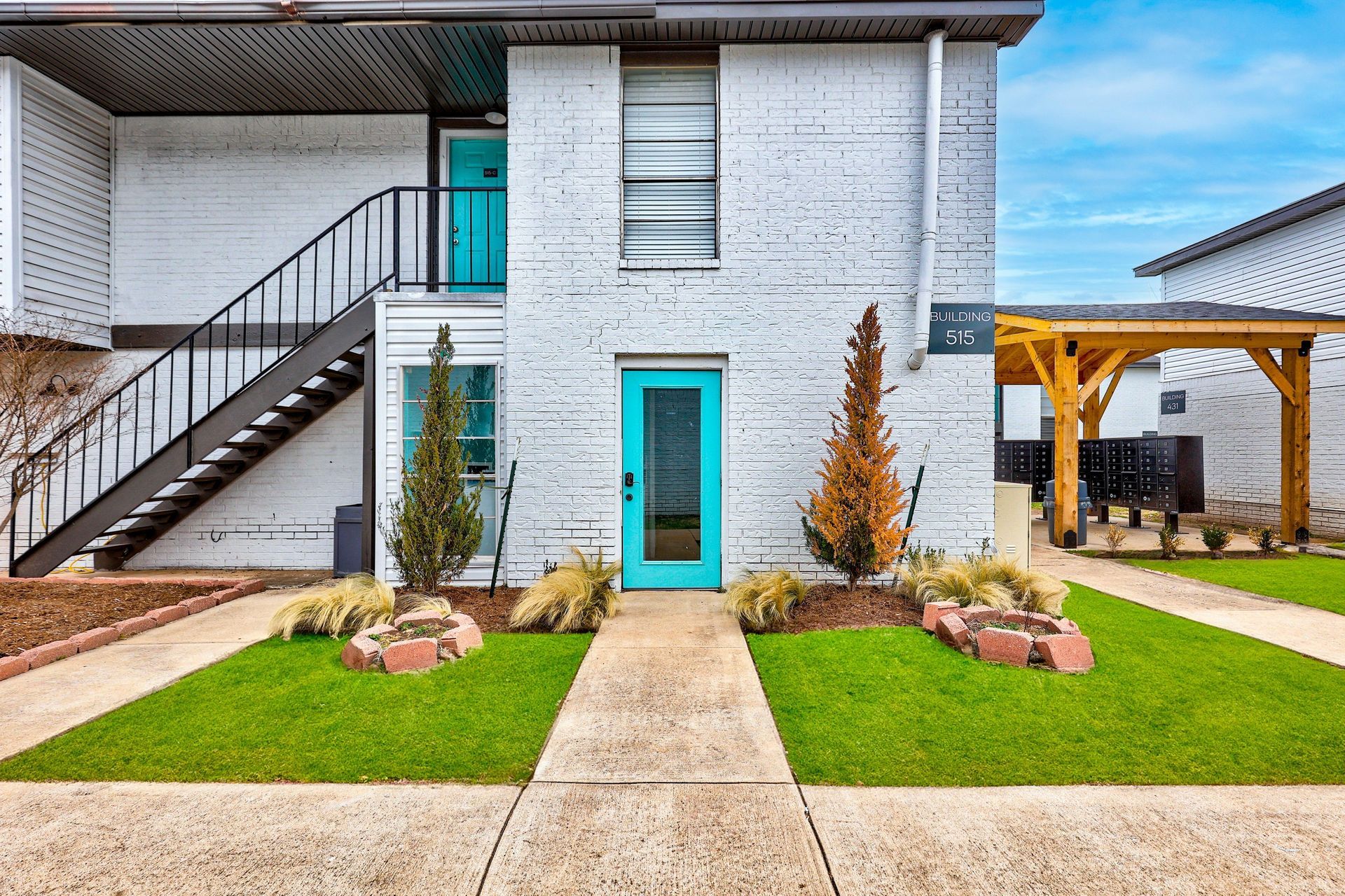 White brick building with teal doors, black stairs, green grass, and walkway.