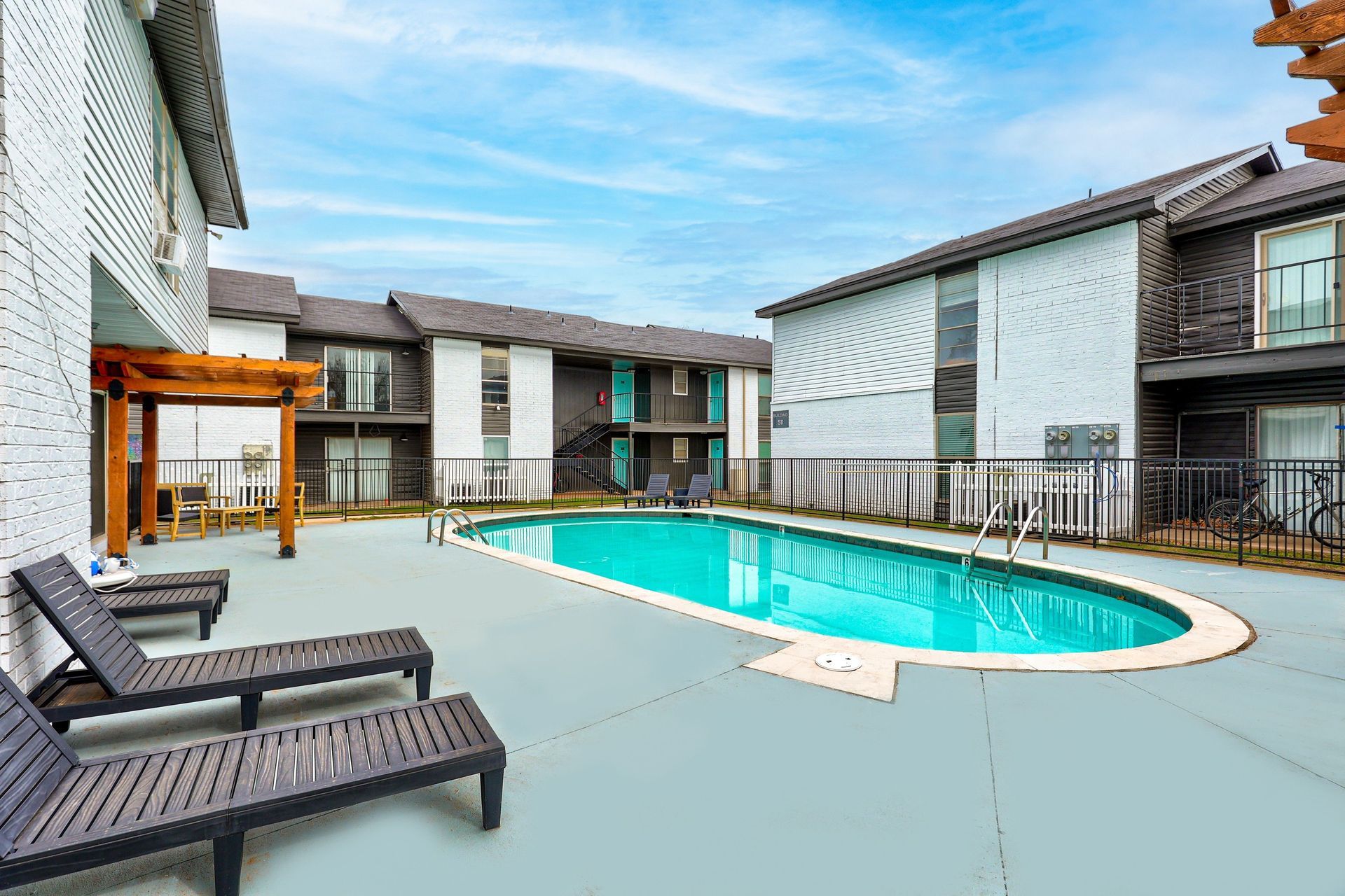 Pool area with lounge chairs, surrounded by two-story buildings with turquoise accents, under a blue sky.