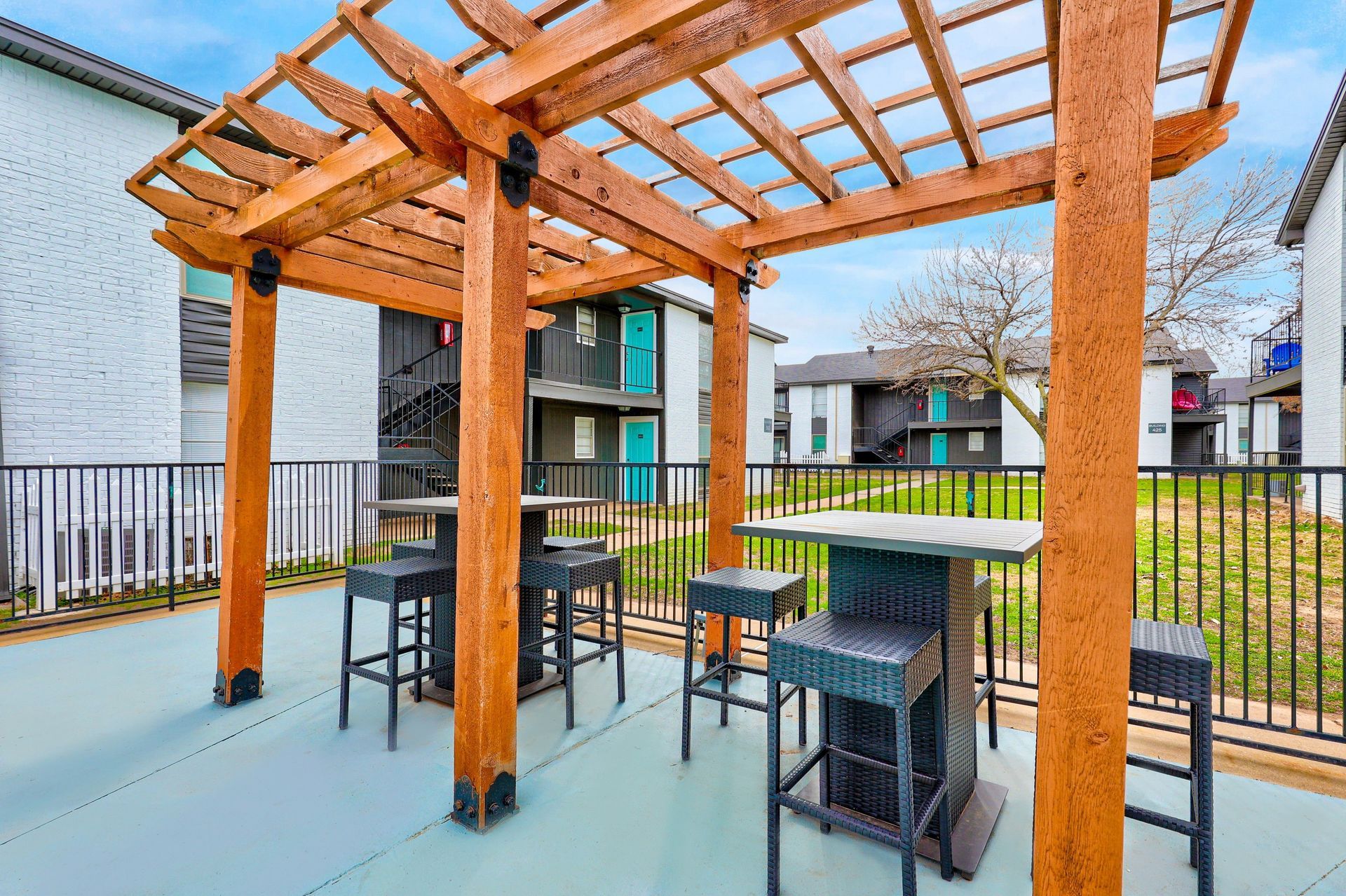 Outdoor seating area with pergola and high-top tables and stools. Buildings in the background.