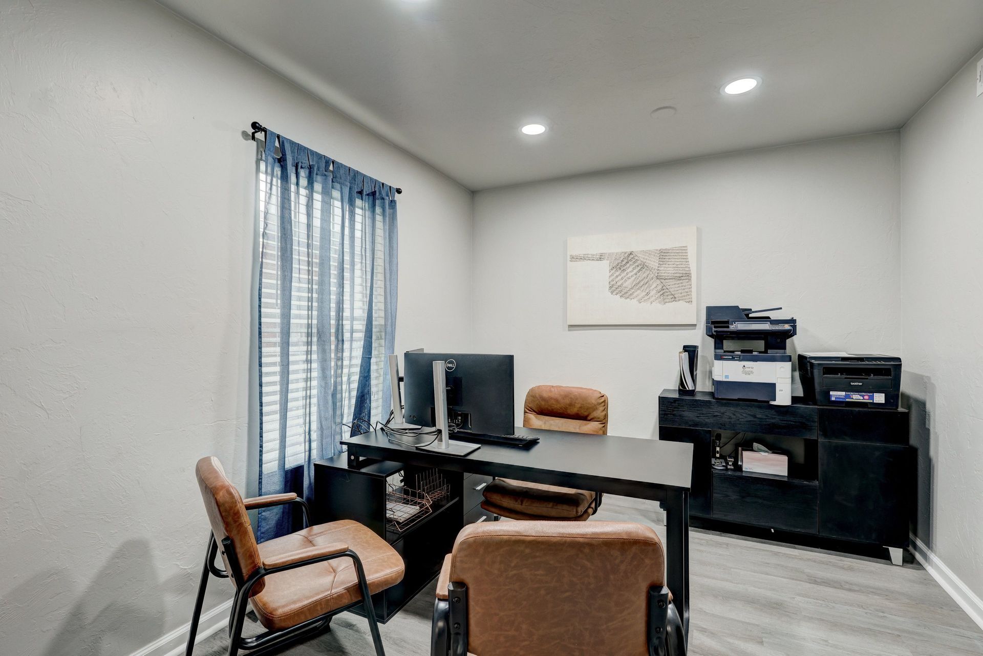 Office with desk, computers, chairs, printers, and a window with blue curtains.