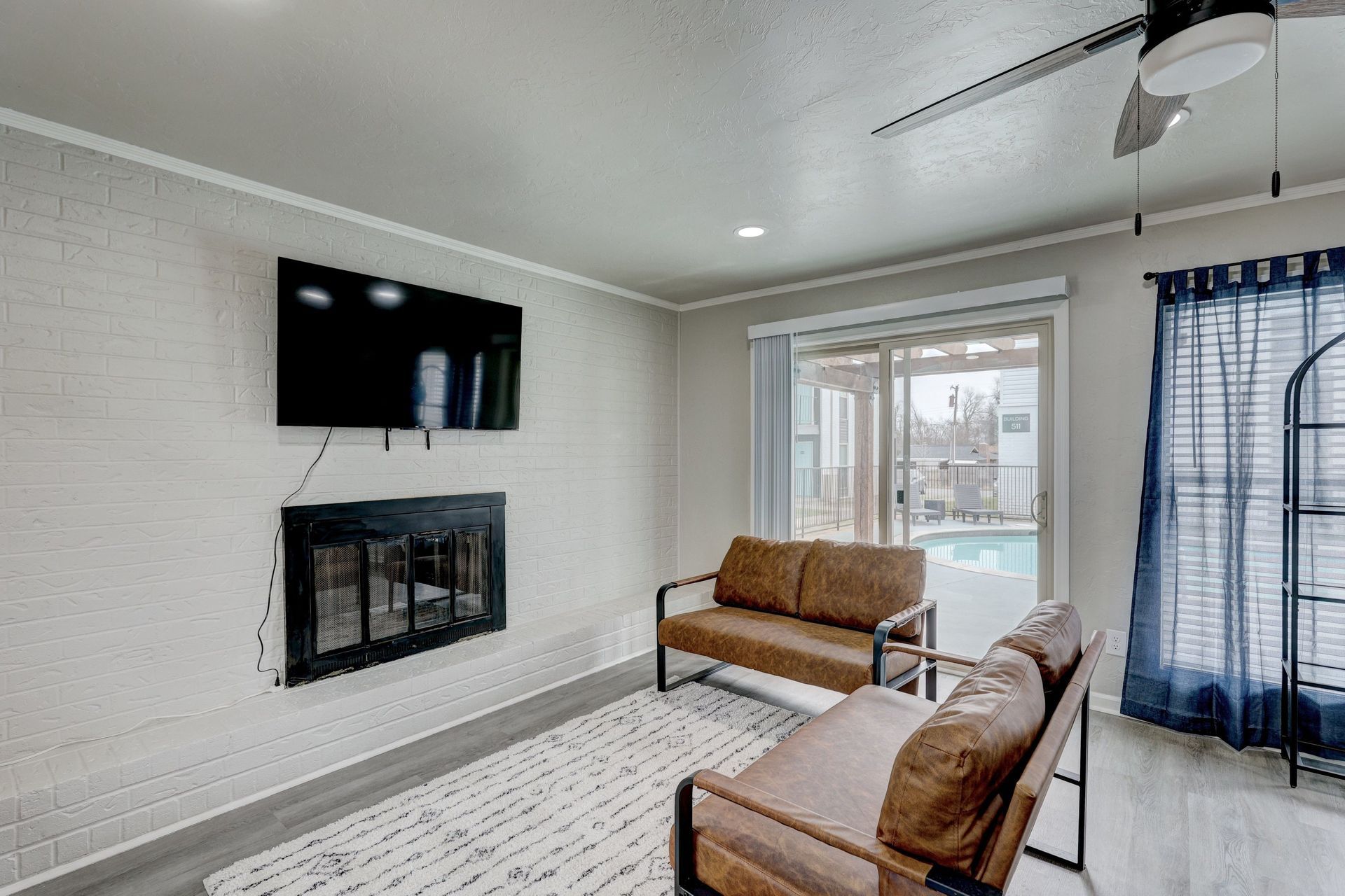 Living room with fireplace, TV, two couches, and a sliding glass door leading to a pool area.