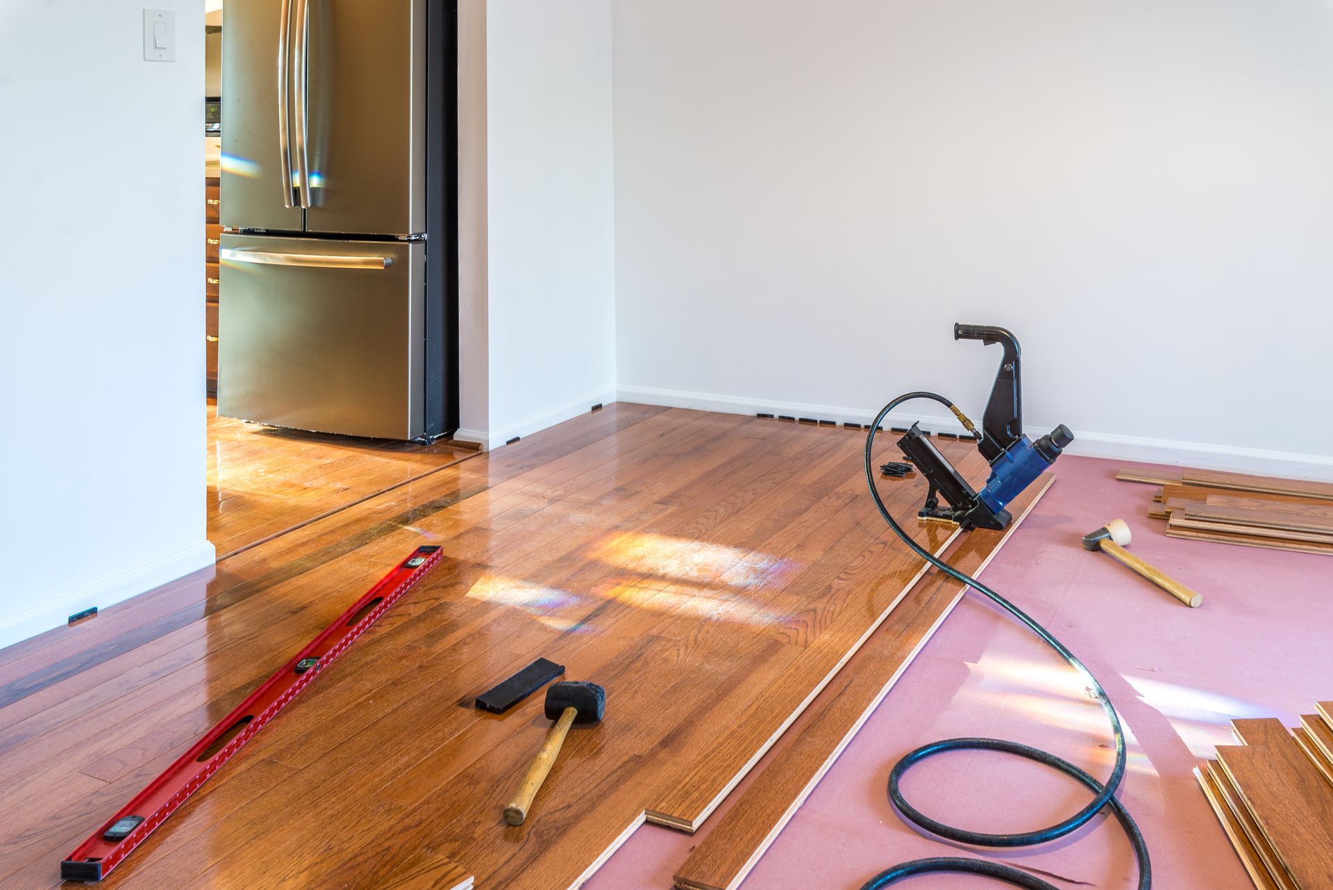 A hardwood floor installation in progress with tools, planks, and underlayment in an empty room