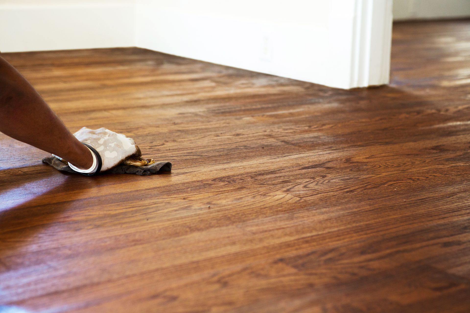 Hand wiping a hardwood floor with a cloth during cleaning or polishing inside a room.