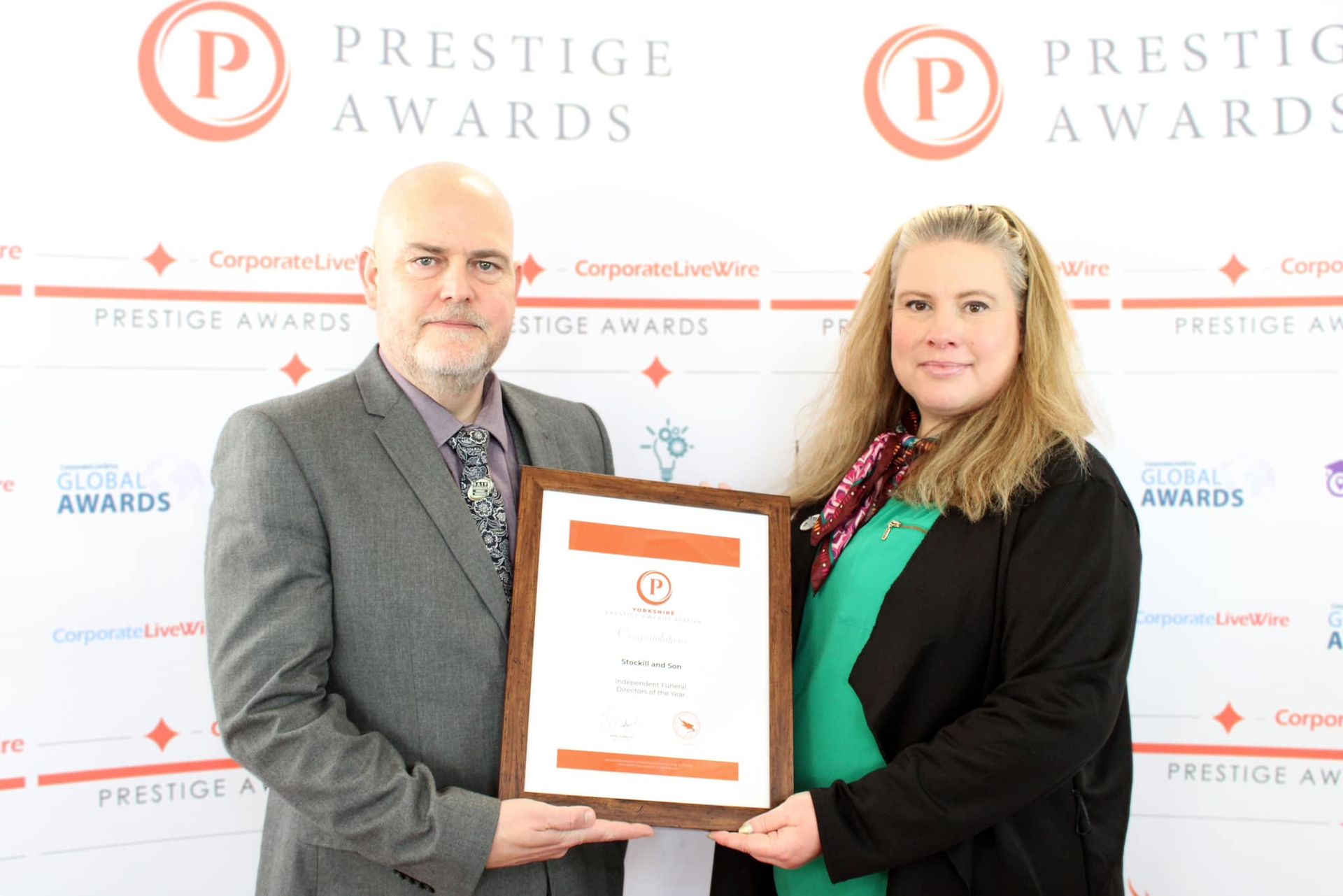 A man and a woman are holding a certificate in front of a wall that says prestige awards.