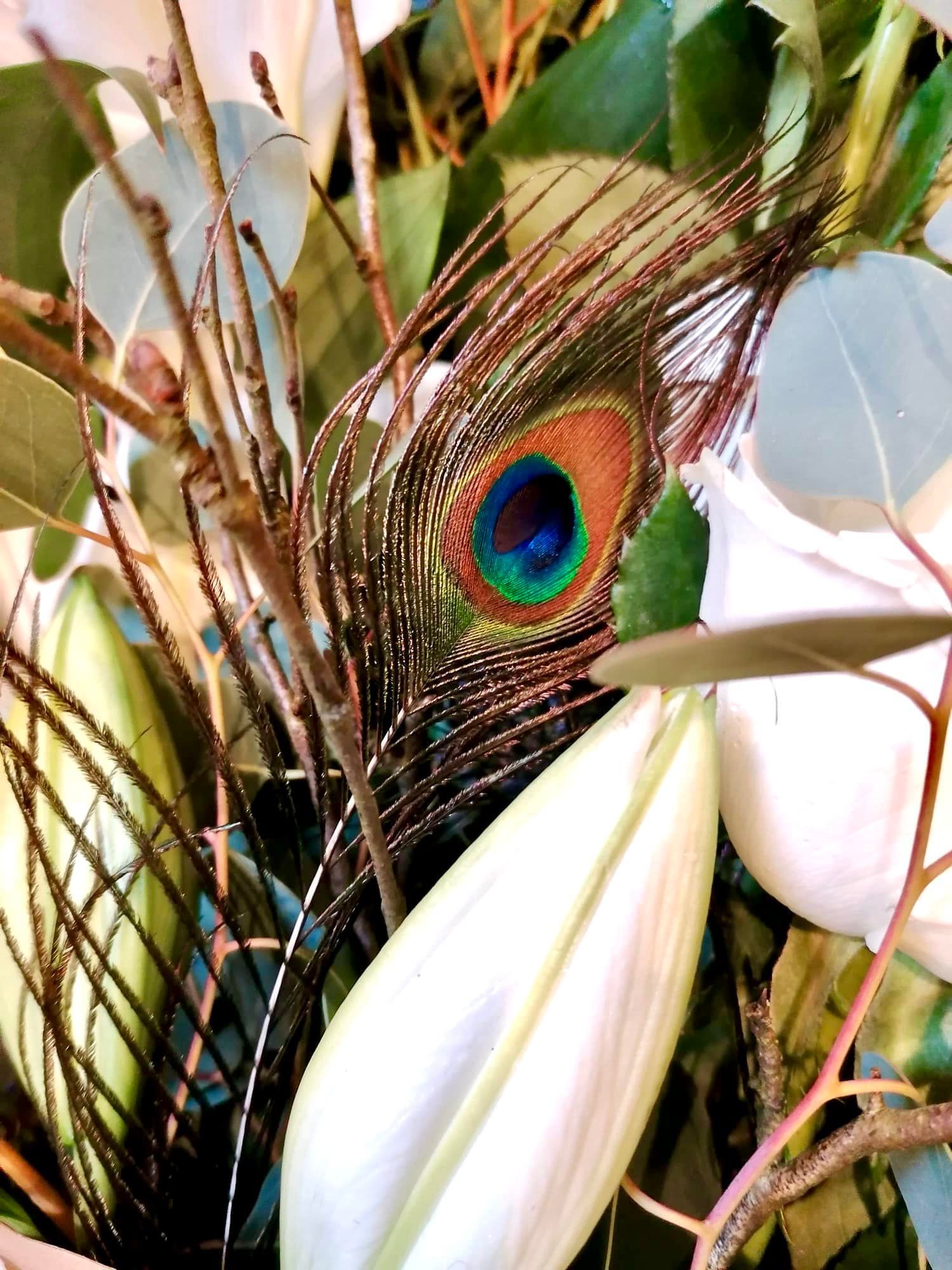 A close up of a peacock feather in a bouquet of flowers