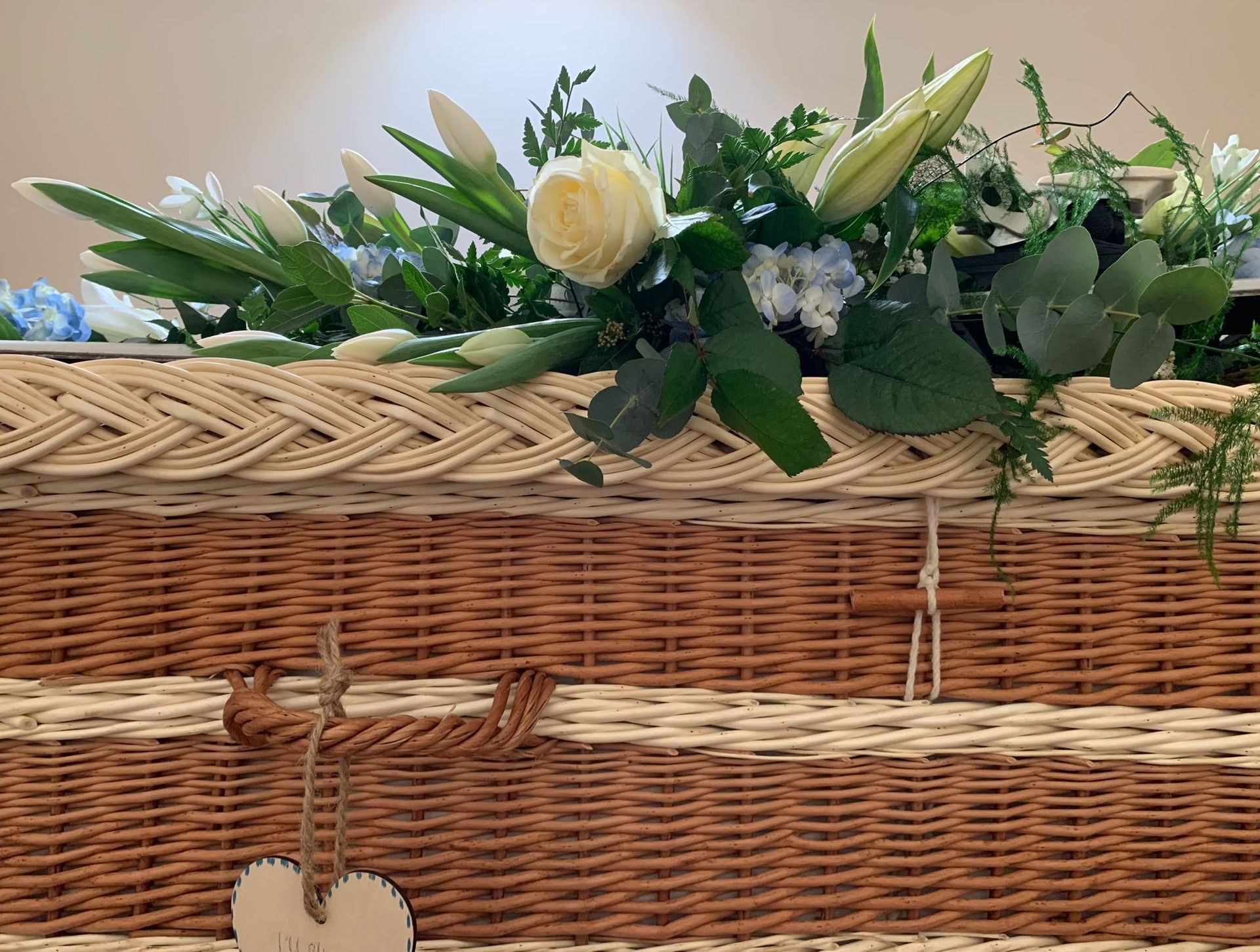 A wicker coffin with flowers and a heart hanging from it.