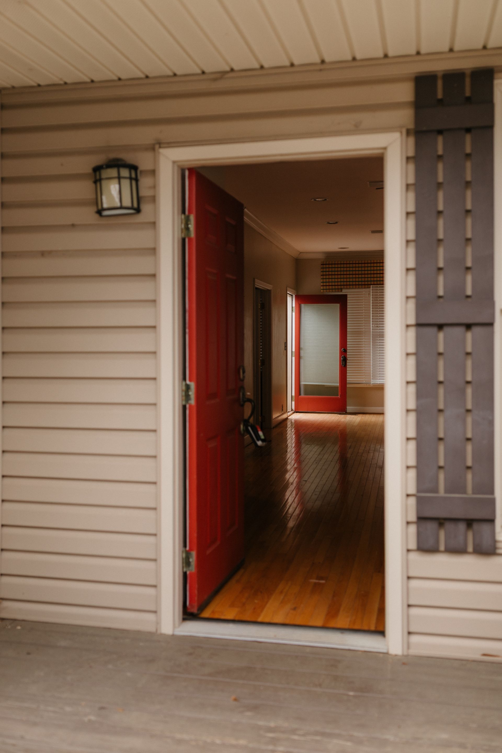 A red door is open on a porch of a house