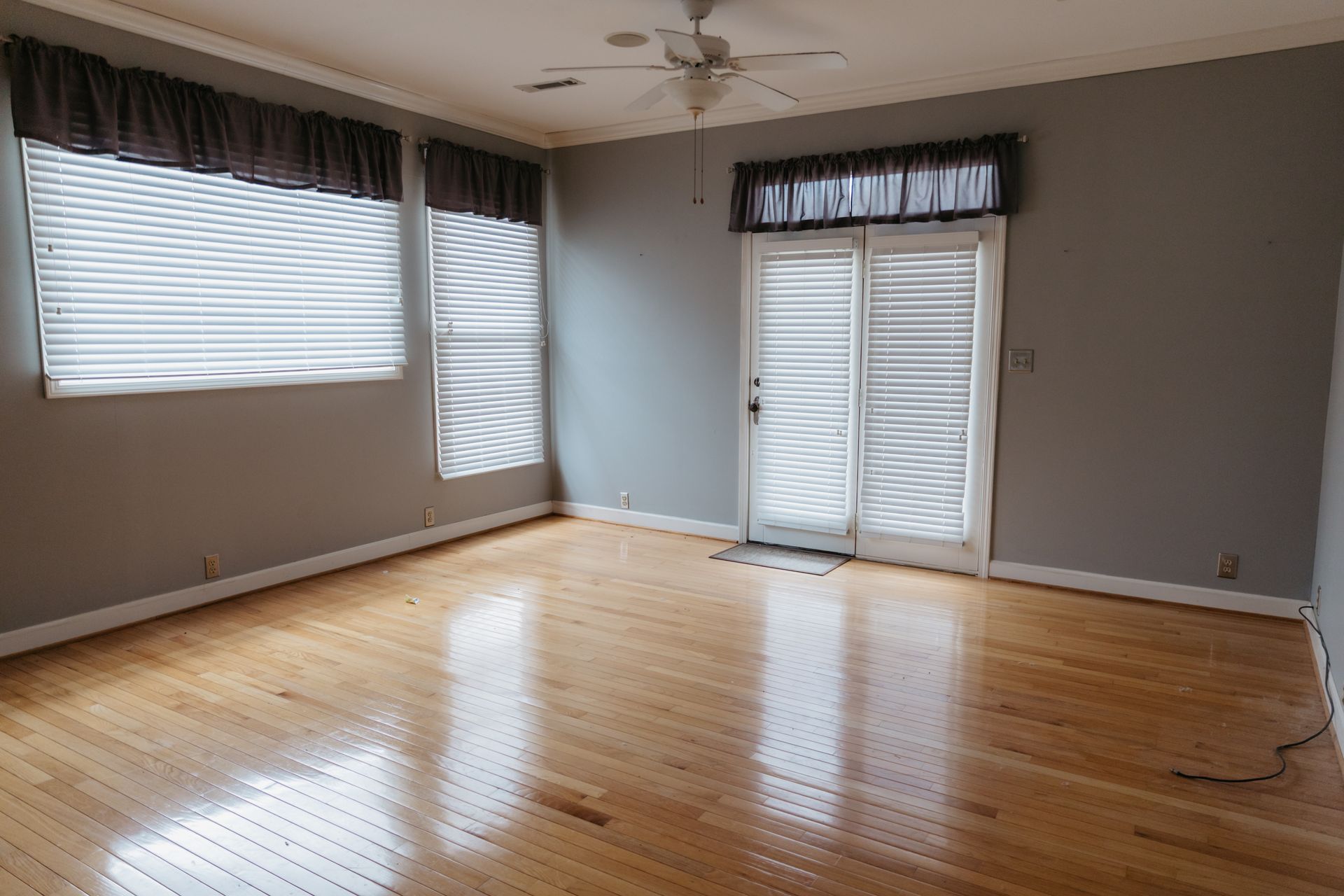 An empty living room with hardwood floors and a ceiling fan.