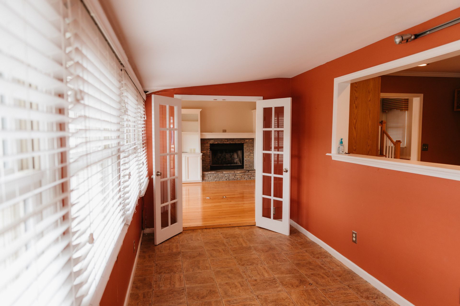An empty living room with red walls and white blinds and a fireplace.