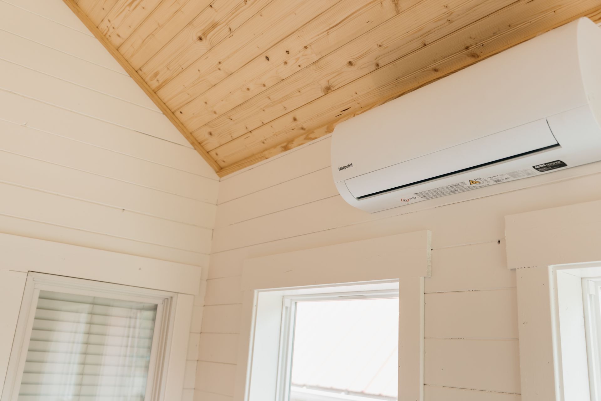 A white air conditioner is hanging from the ceiling of a room next to a window.