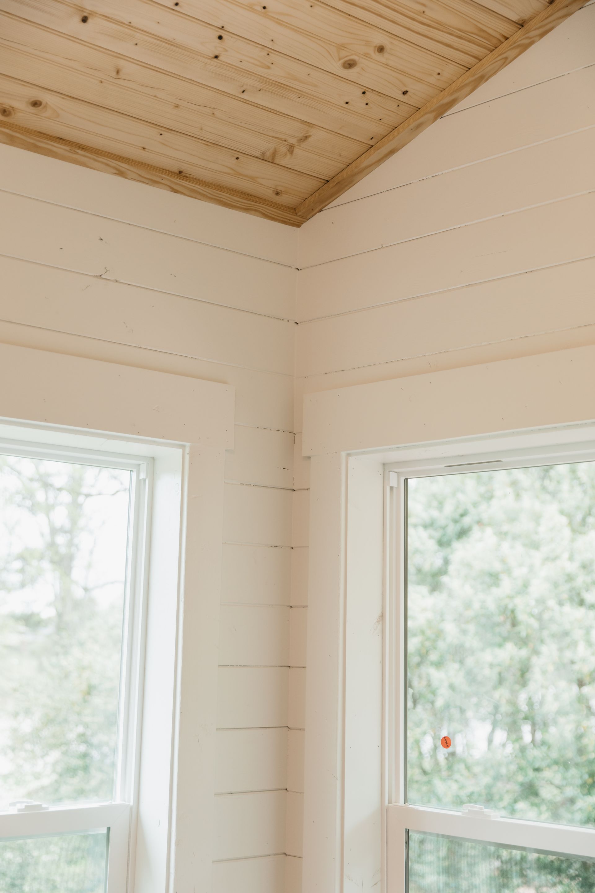 A room with white walls and a wooden ceiling and two windows.